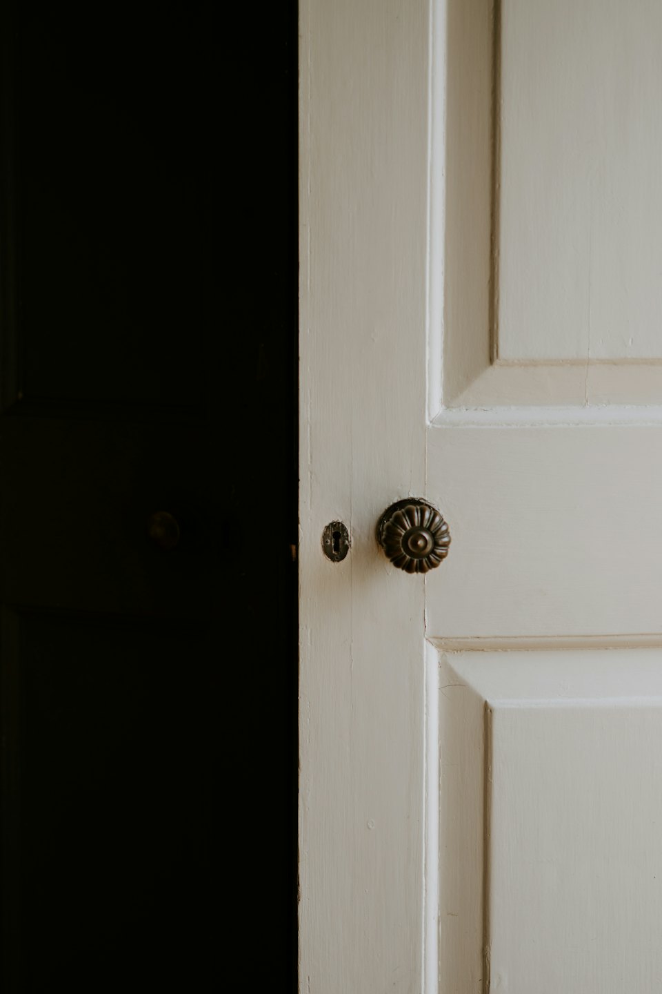 Puerta de madera pintada ligeramente abierta con pomo y cerradura de latón.