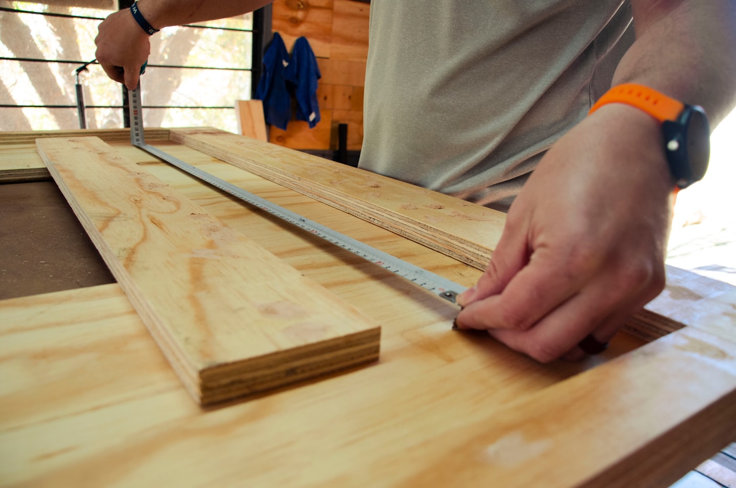 Manos midiendo madera contrachapada con una cinta métrica.