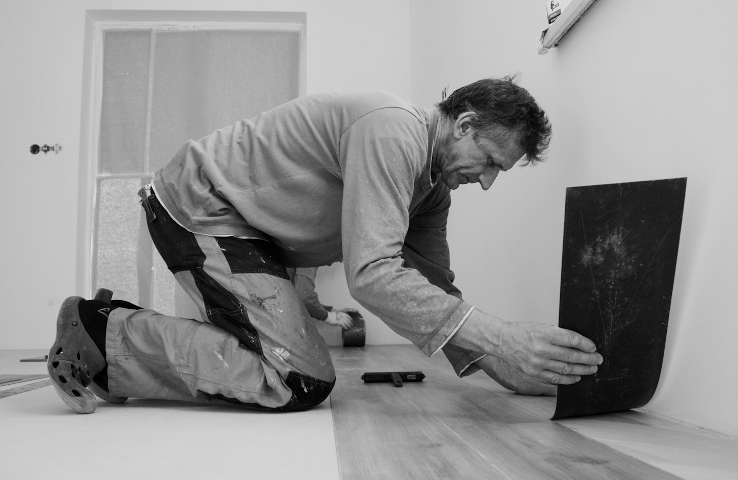 Hombre instala nuevo suelo de aspecto madera en una habitación de paredes blancas.